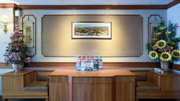 A reception desk with a framed cityscape picture, a vase of sunflowers, and a floral arrangement.