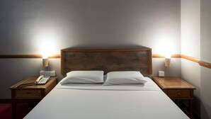 Een keurig opgemaakt bed met witte lakens en twee kussens, aan weerszijden van houten nachtkastjes met lampen.