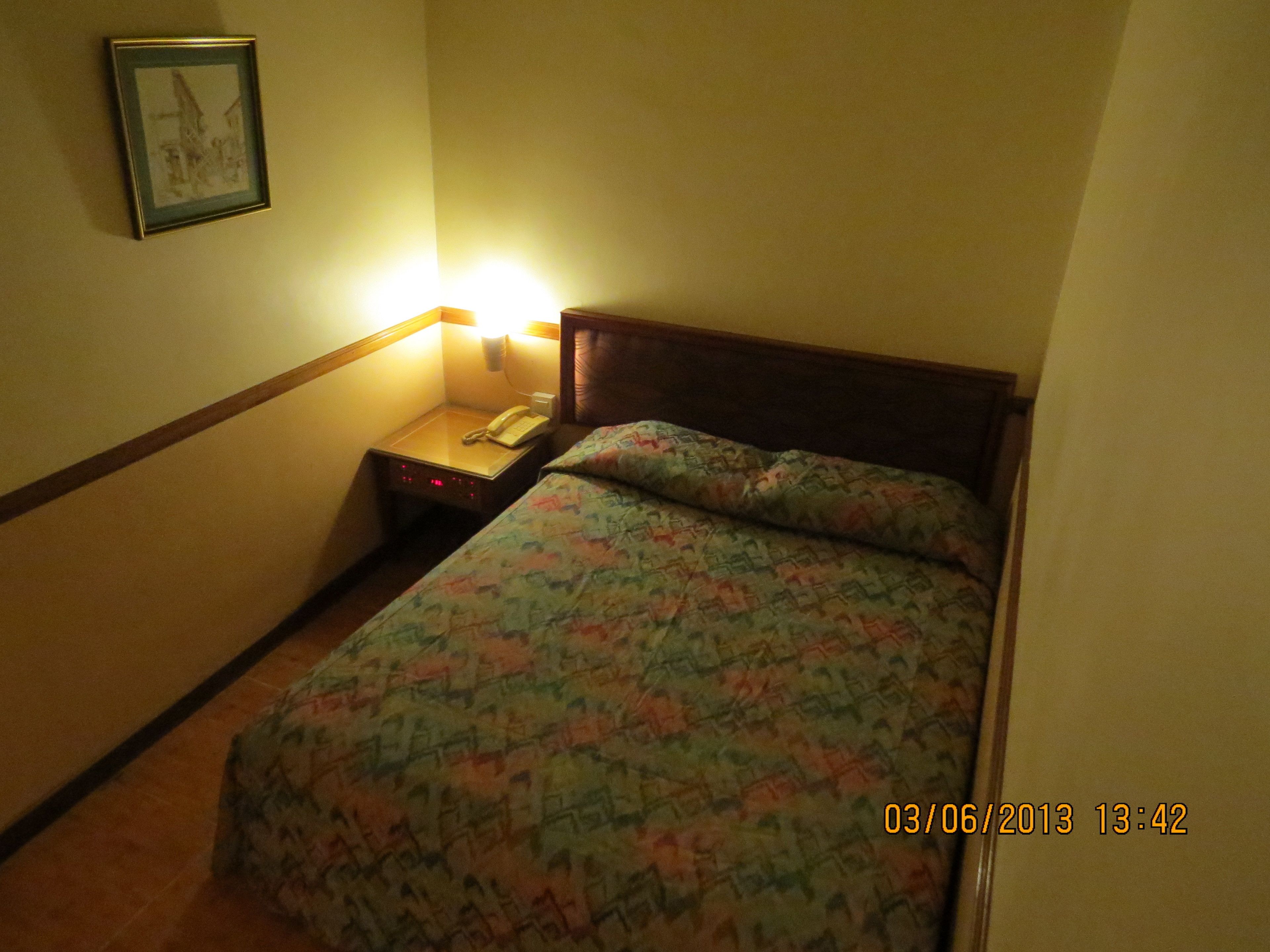 A hotel room with a bed, a nightstand with a phone, and a wall-mounted light.