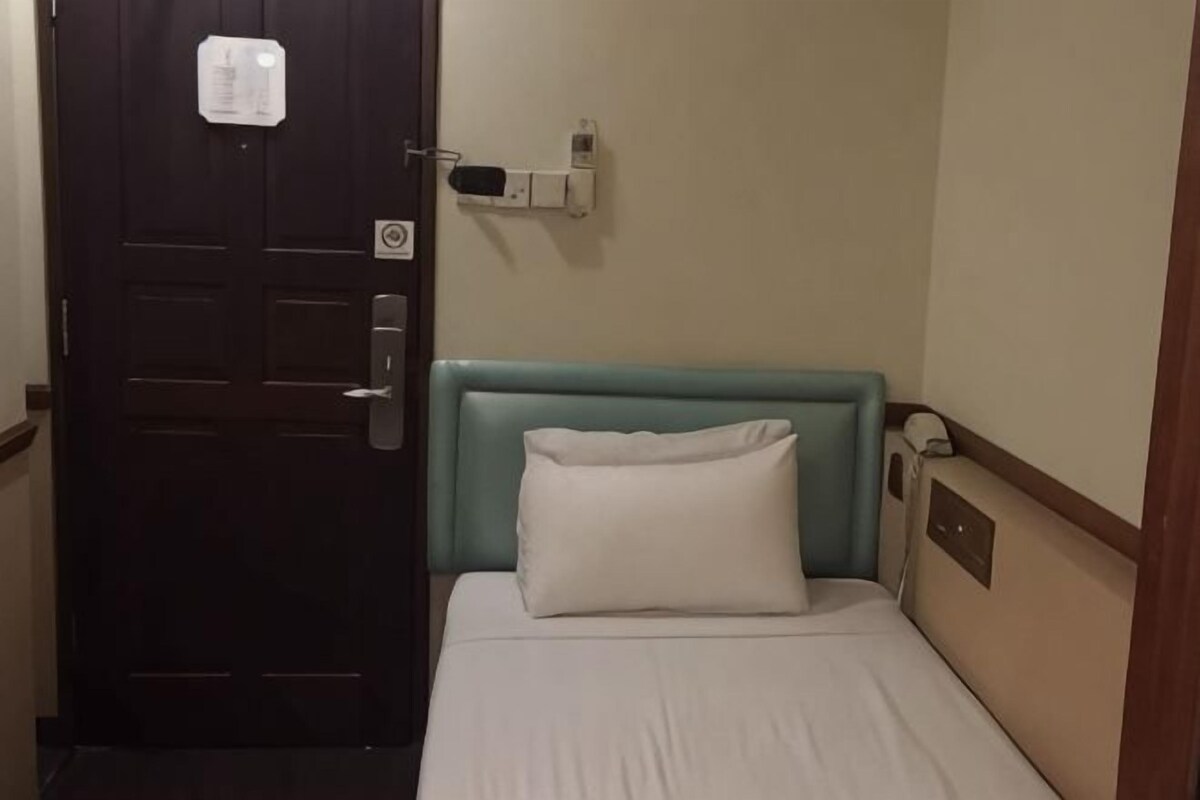 A hotel room with a bed, a door, a thermostat, and a wall-mounted device.