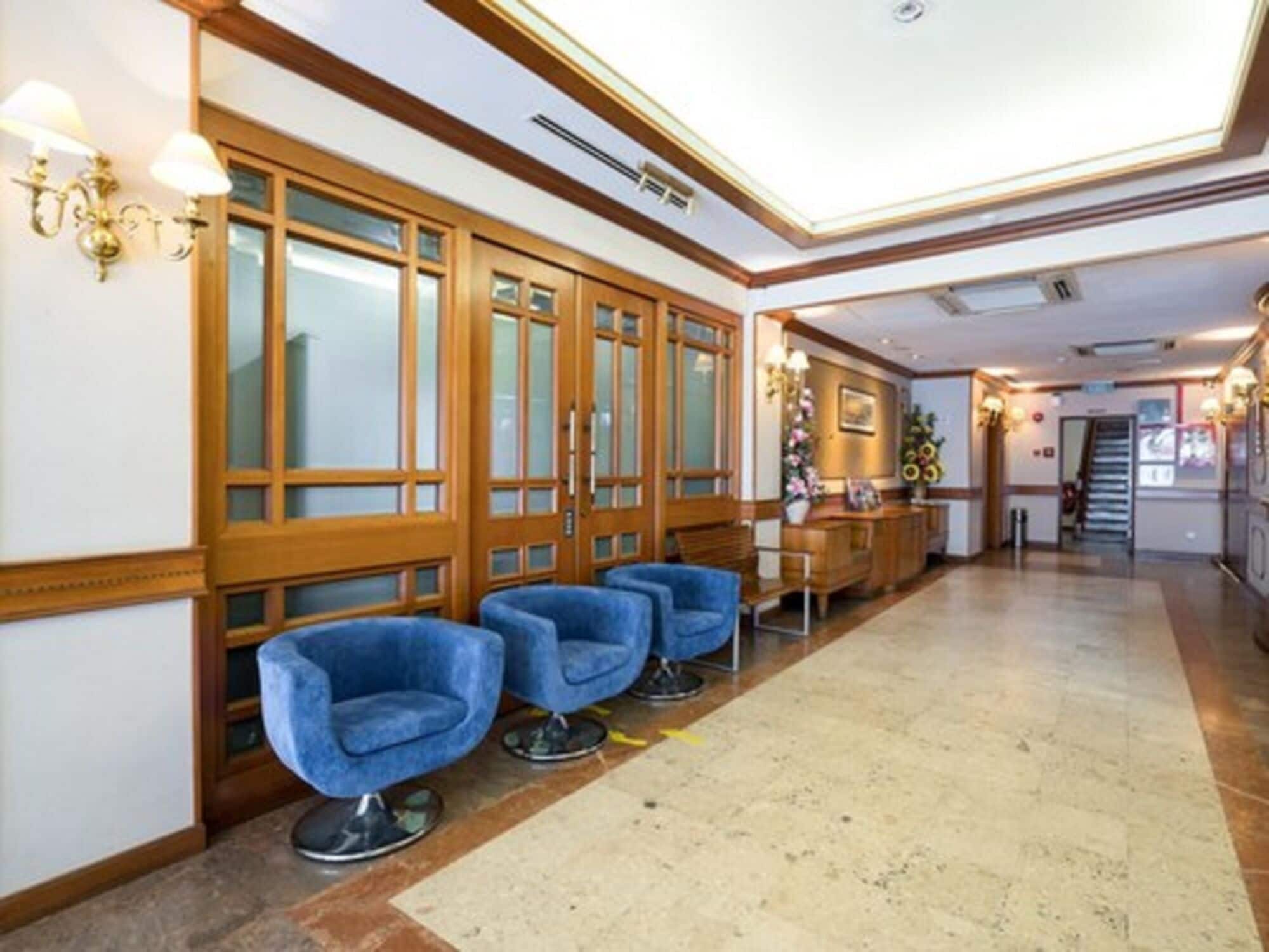 A hotel lobby with wooden paneling, a reception desk, and blue chairs.