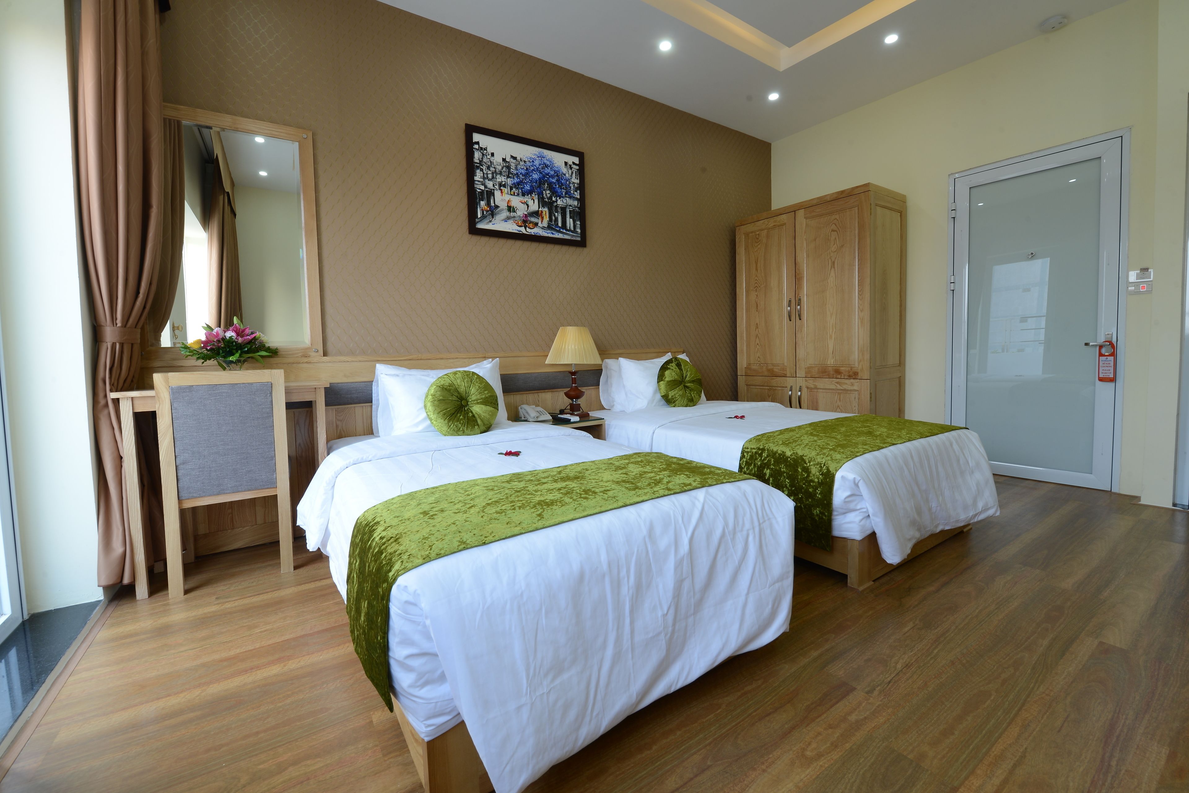 A hotel room with two beds, a desk, a mirror, a painting, and a wardrobe.