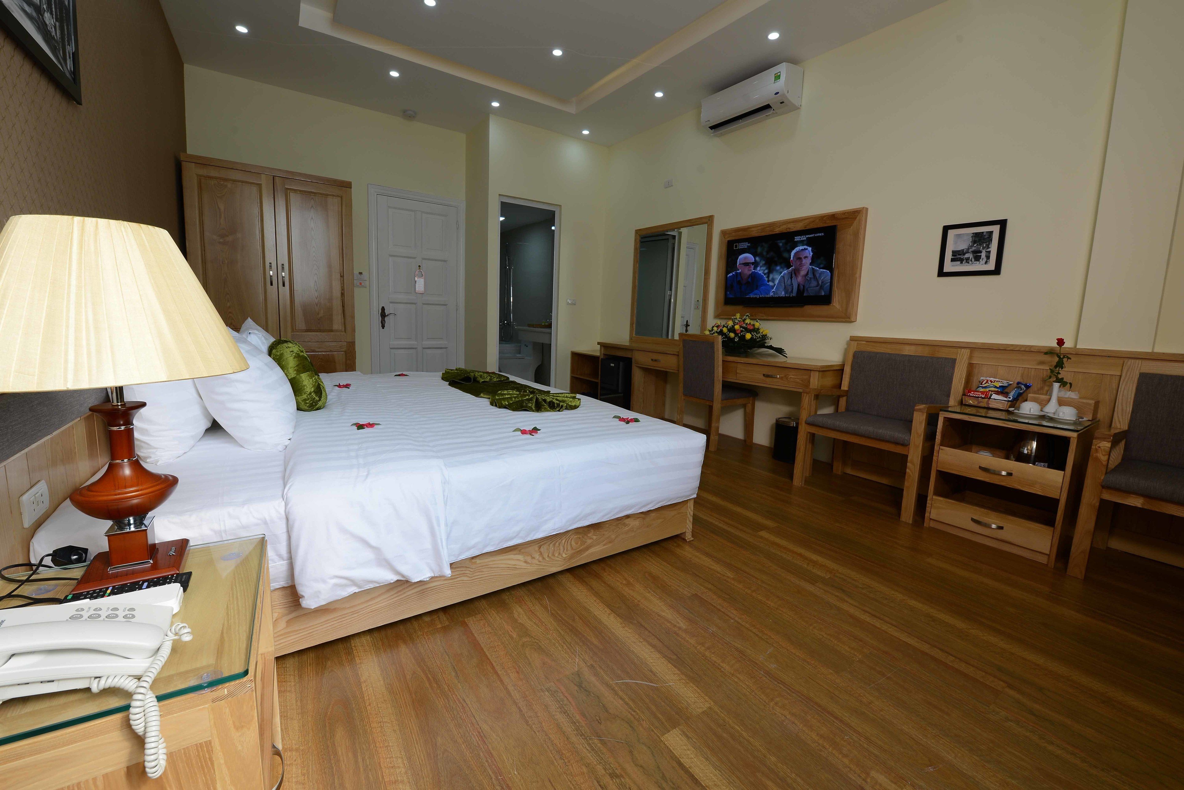 A hotel room with a bed, bedside table with a lamp, a desk with a chair, a television, and a wardrobe.