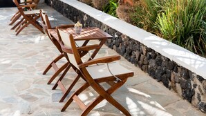 A patio with stone flooring, wooden chairs, and a thatched roof. - Memento Perissa (Santorini)