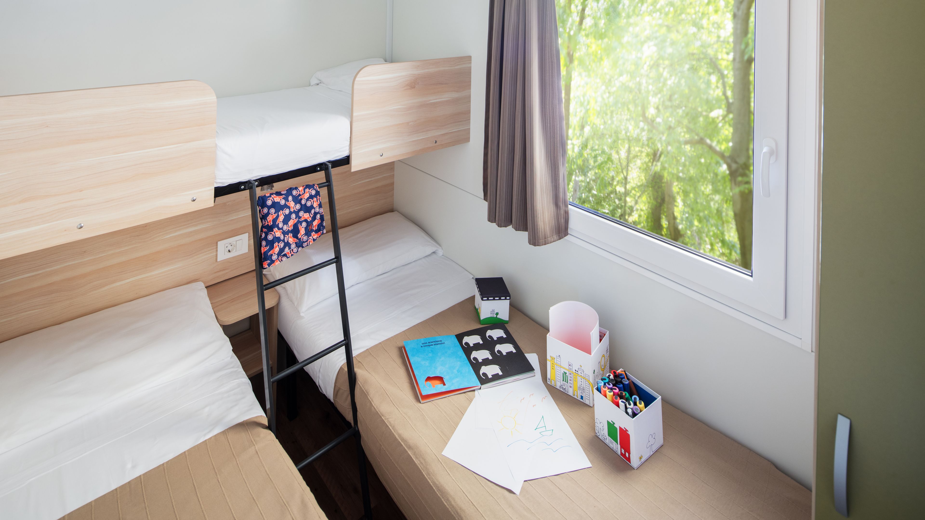 A bunk bed room with a window, a ladder, a book, and a box of markers.