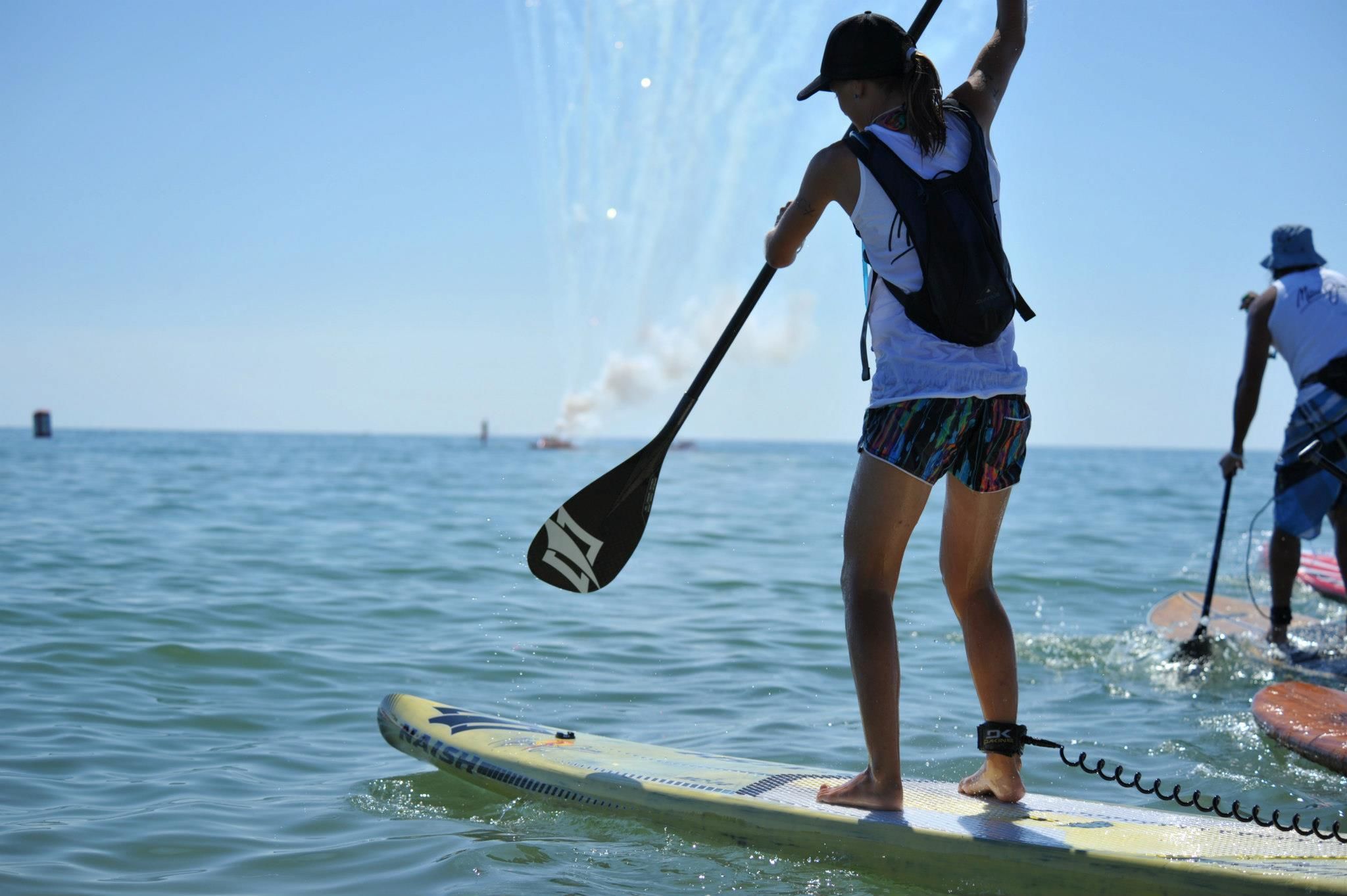 A person standing on a paddleboard in the water, holding a paddle.
