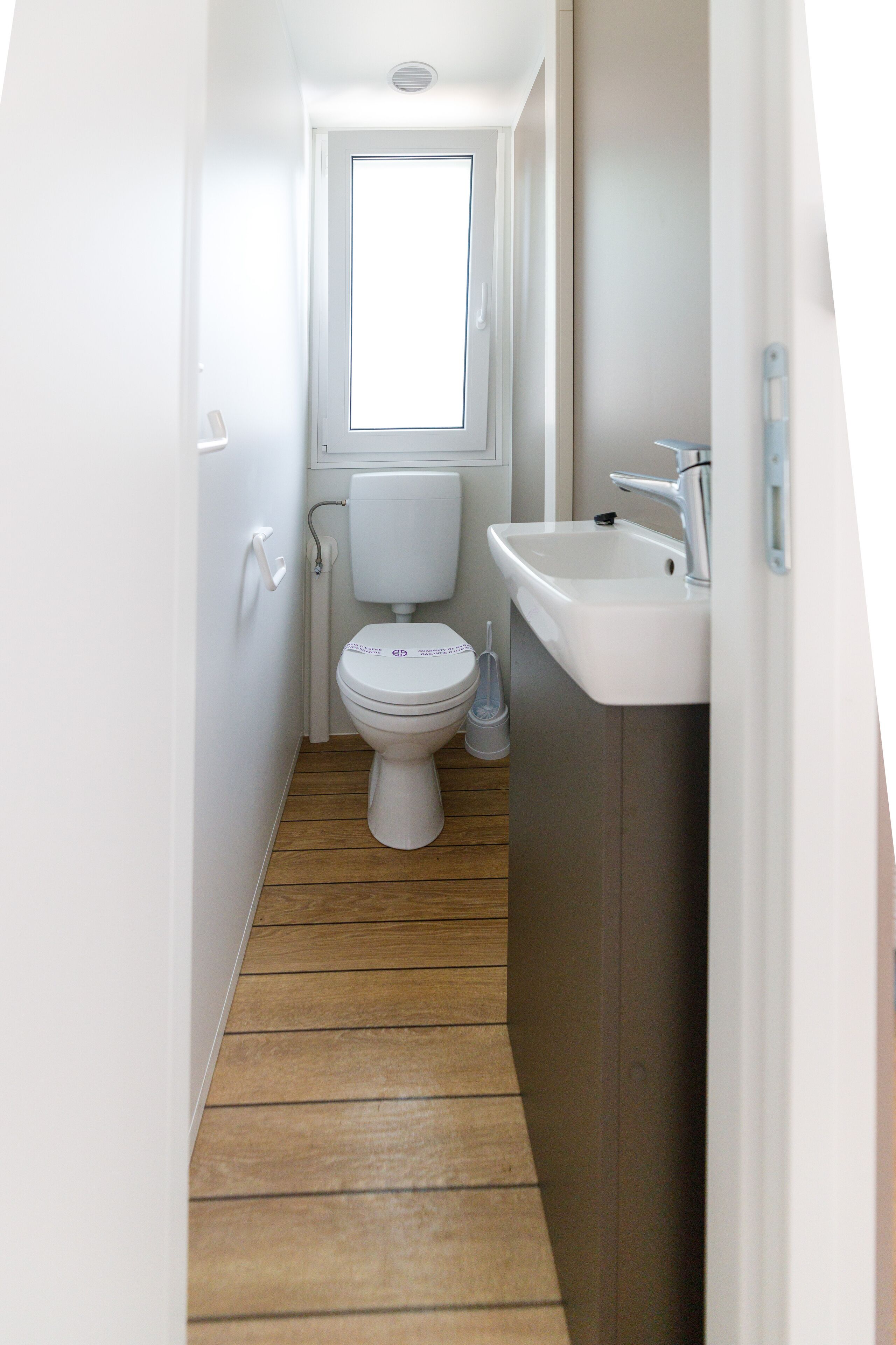 Een kleine badkamer met toilet, wastafel en raam.
