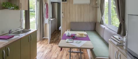 A compact kitchenette with a sink, a dining area with a table and bench, and a window with curtains.