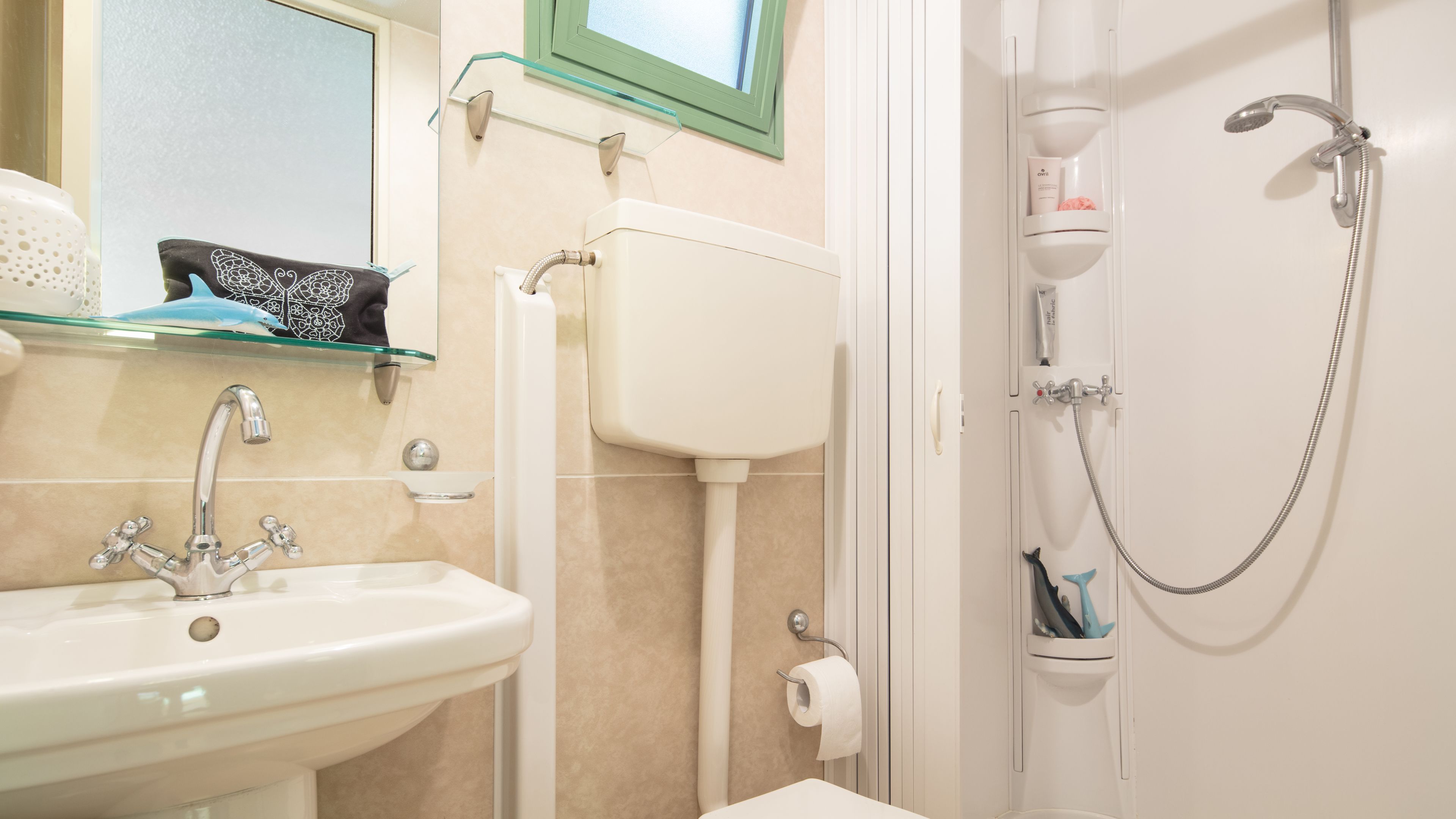 A bathroom with a white sink, a glass shelf with a decorative item, a toilet, and a shower with a hose.