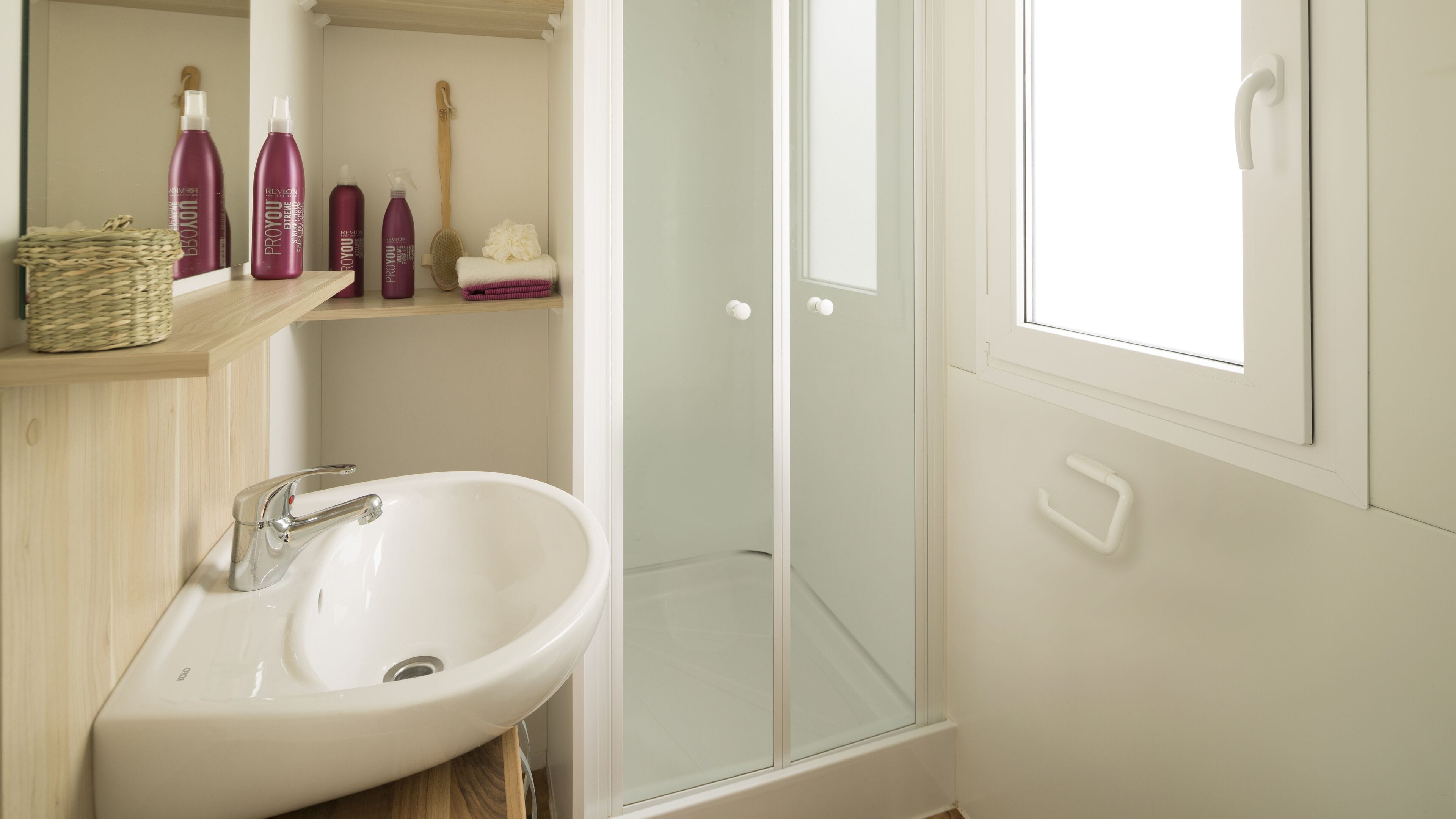 A bathroom with a white sink, a glass shower enclosure, and shelves with toiletries.