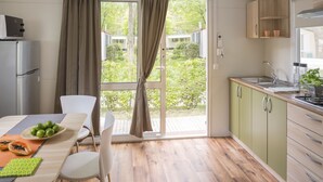 Una cocina moderna con un amplio ventanal corredera que da a un jardín, una mesa de comedor con sillas y un refrigerador.