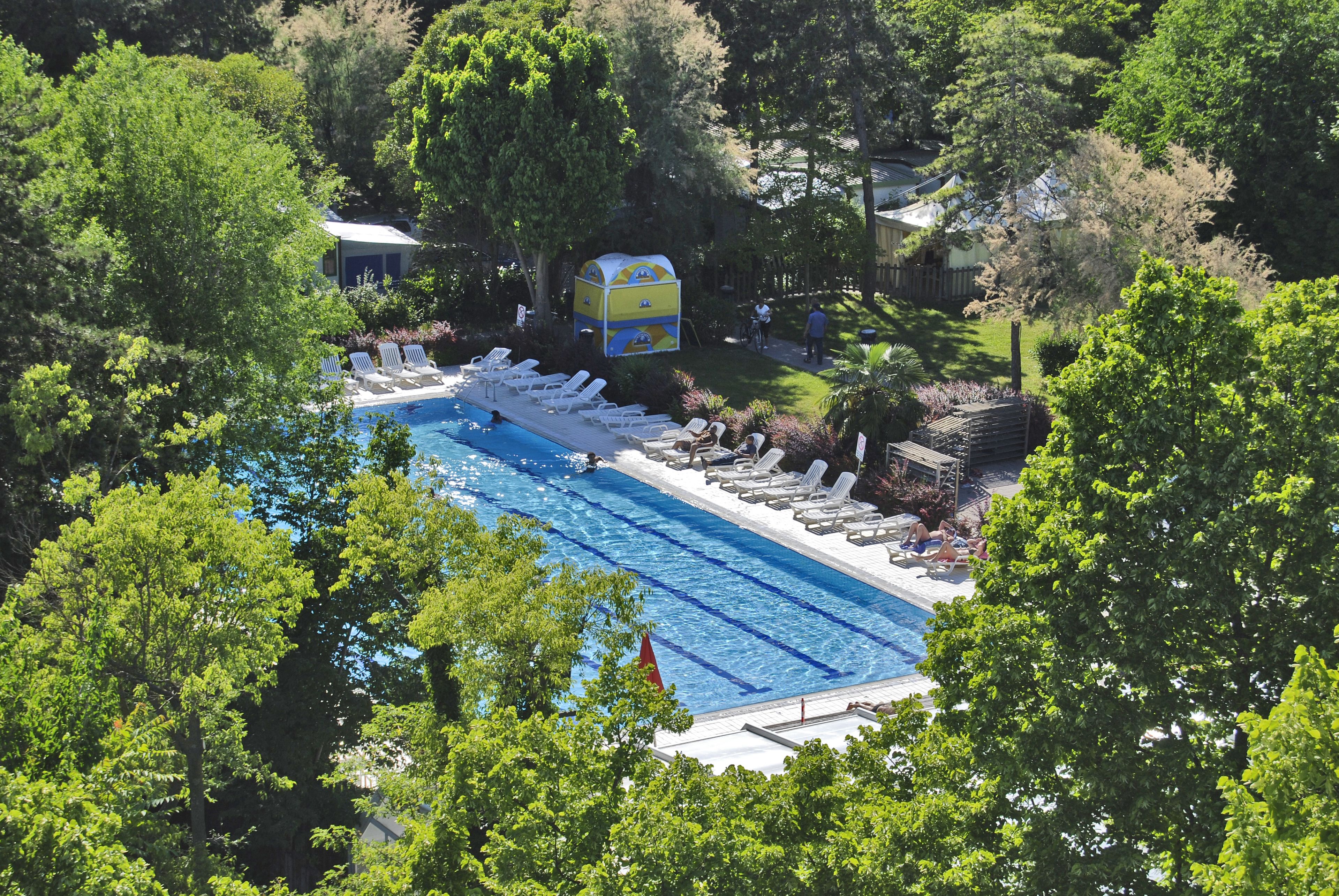 A swimming pool with lounge chairs and a small building, surrounded by trees.