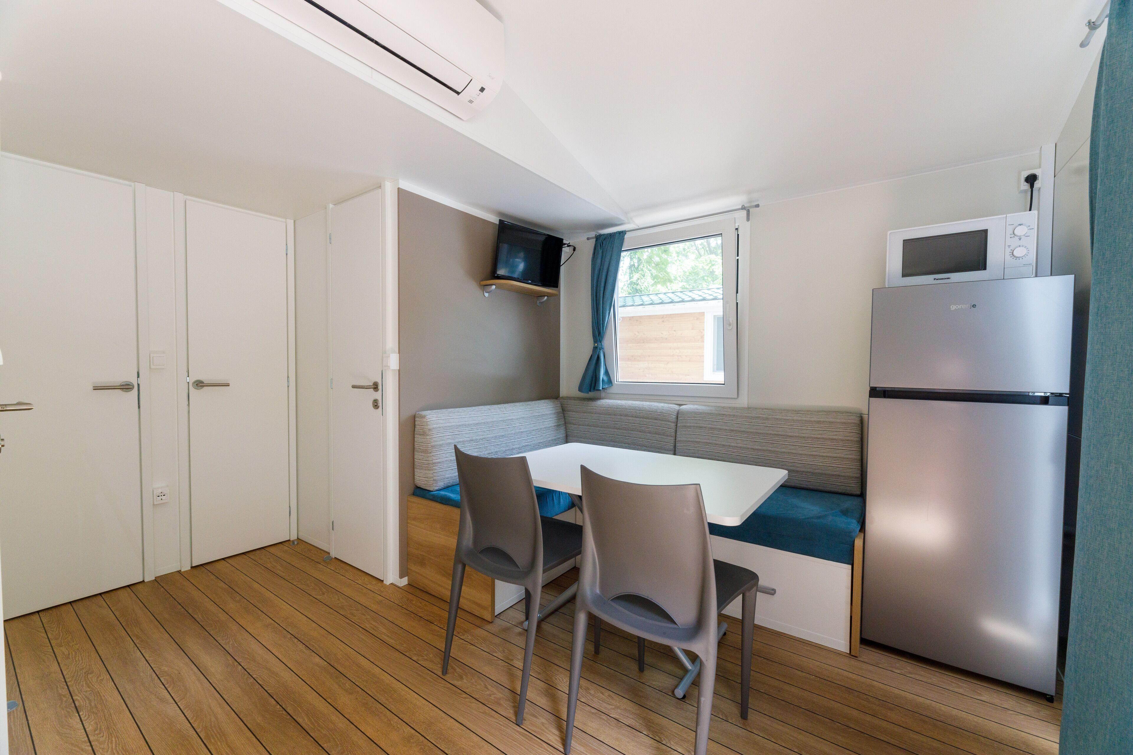 A compact kitchen with a dining table, two chairs, a built-in bench, a microwave, and a refrigerator.