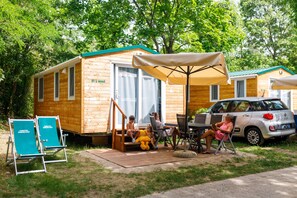 A wooden cabin with a patio area, outdoor seating, and a car parked nearby. - Camping Sabbiadoro (Lignano Sabbiadoro)