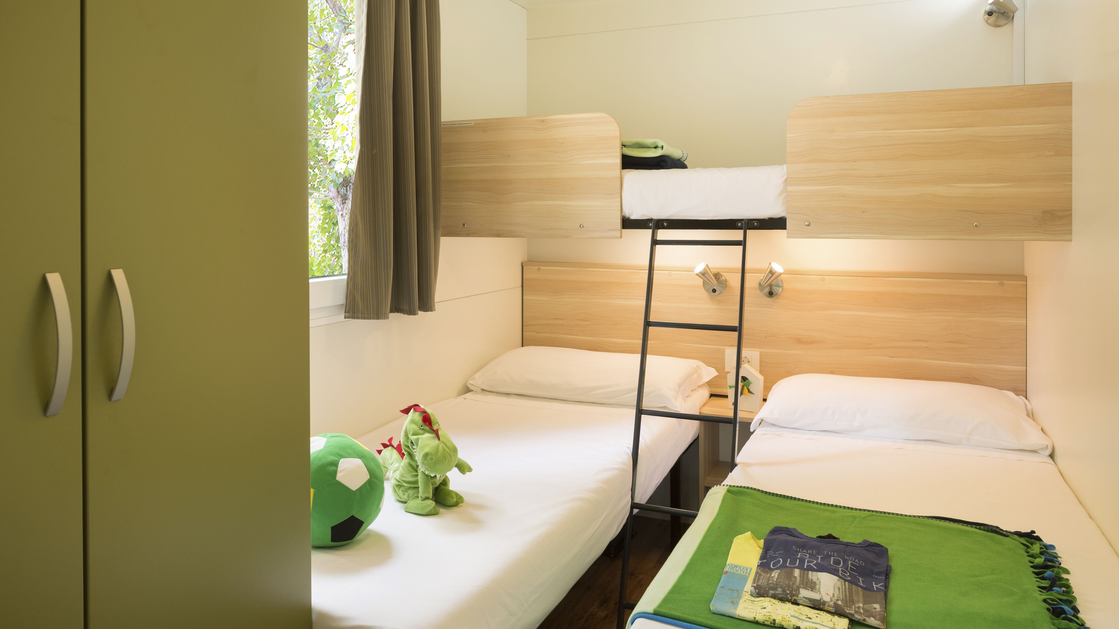 Una stanza del dormitorio con letti a castello, una scala, un cuscino verde e un peluche.