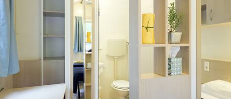 A compact hotel room with a bed, a small desk, a bathroom with a toilet and sink, and a mirror.