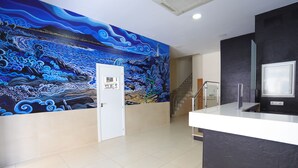 Un espace d’accueil avec une grande fresque murale, un comptoir d’accueil et un escalier.