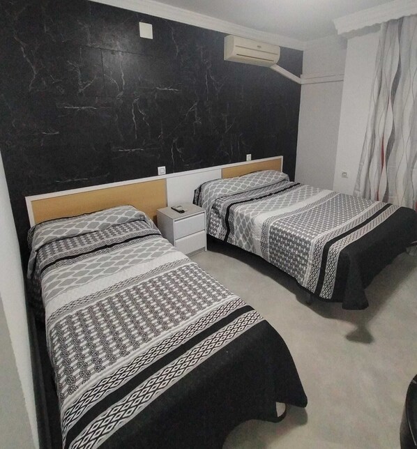 A hotel room with two beds, a marble wall, an air conditioning unit, and a curtain. - Hostal La Campana (La Línea de la Concepción)