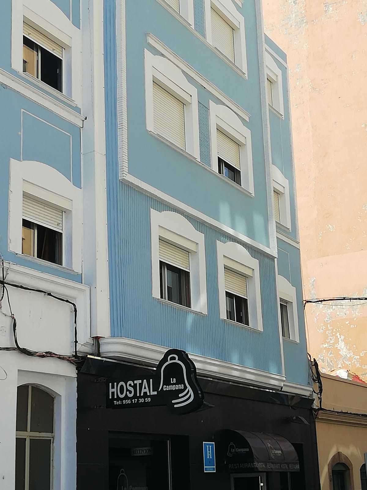 Un edificio de varios pisos con fachada azul y detalles blancos. Se ve un letrero que dice "HOSTAL La Campana", indicando que es un hostal.