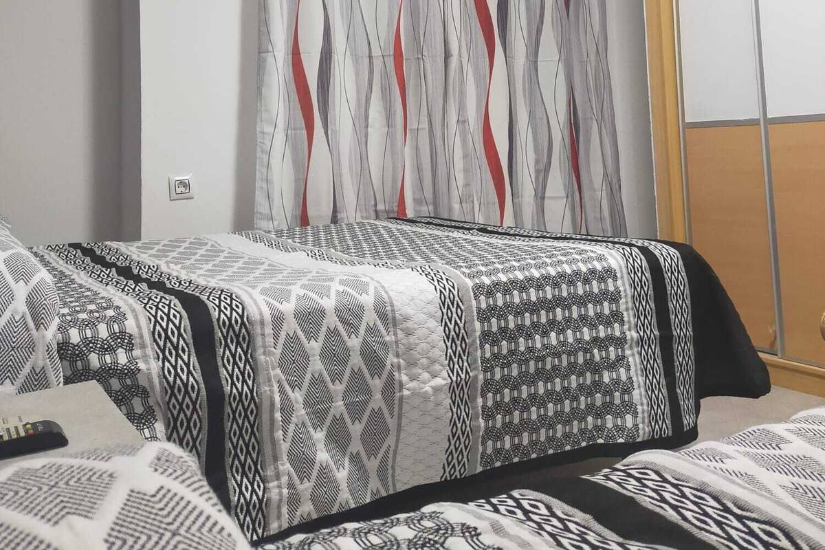 Una habitación de hotel con dos camas, un ventanal con cortinas estampadas y un armario de madera.