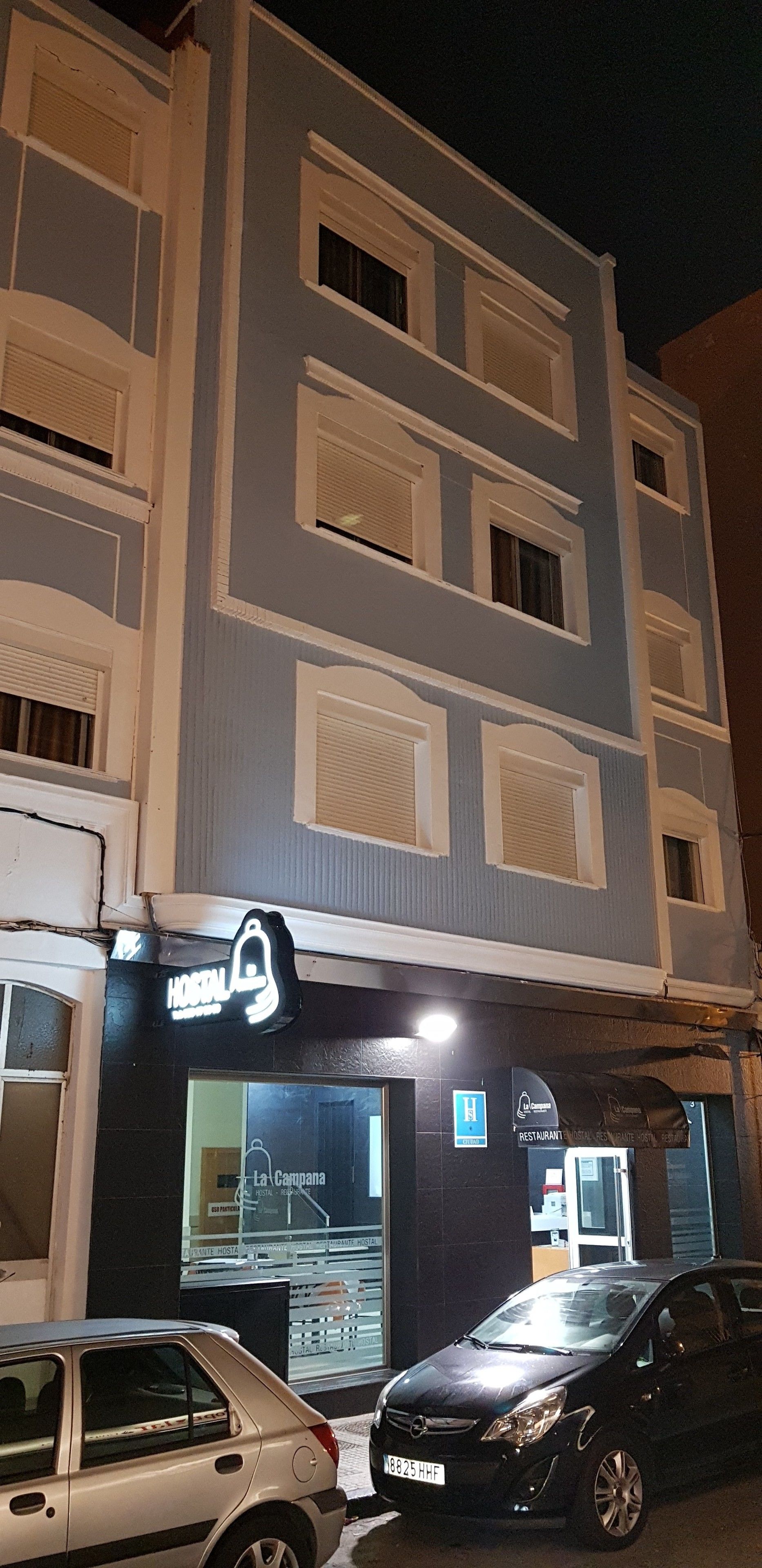 Un hotel con un cartel que indica que alberga un restaurante y un hospital. Hay coches estacionados frente al establecimiento.