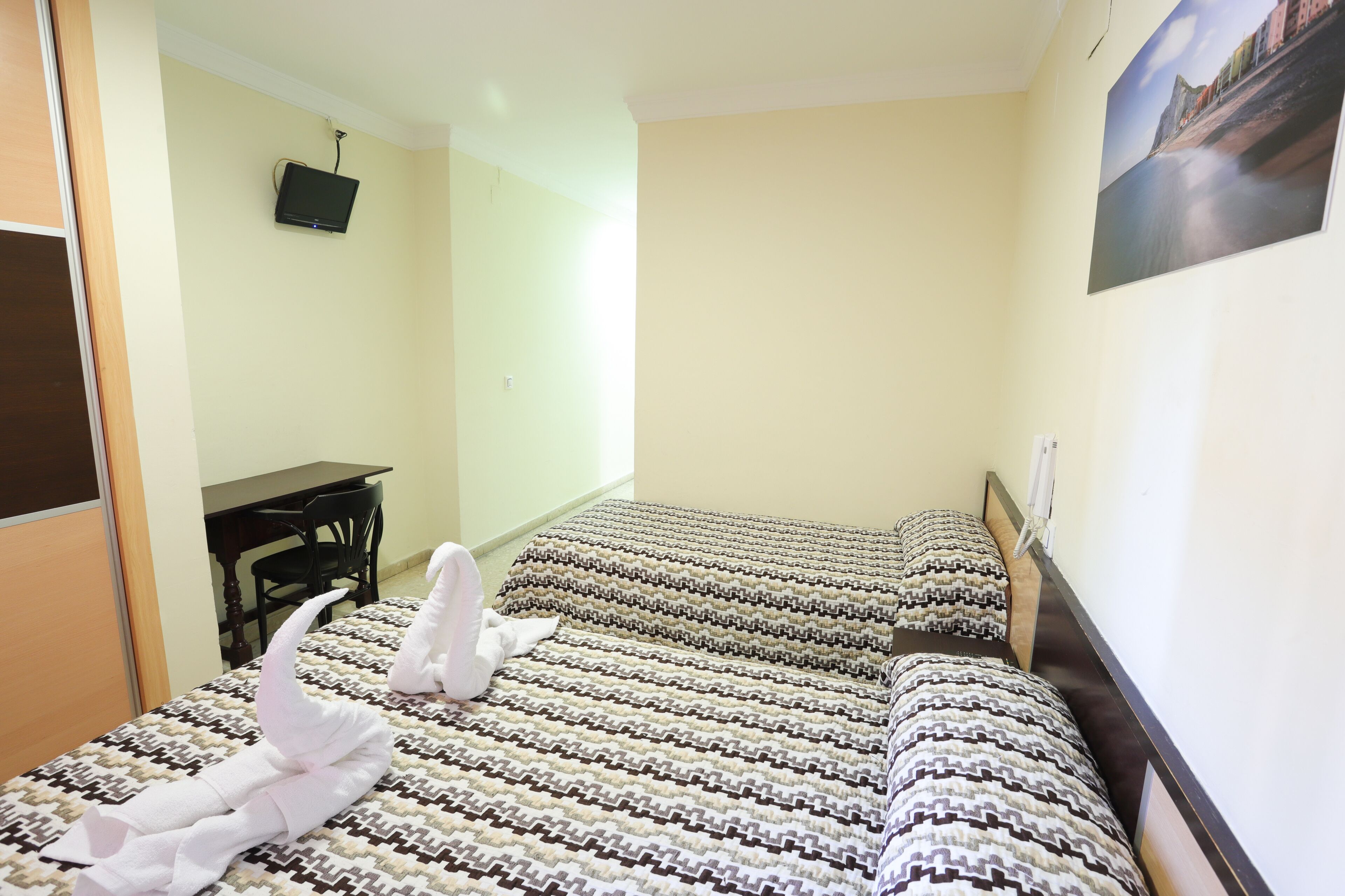 Een hotelkamer met twee bedden, een bureau en een televisie aan de muur.