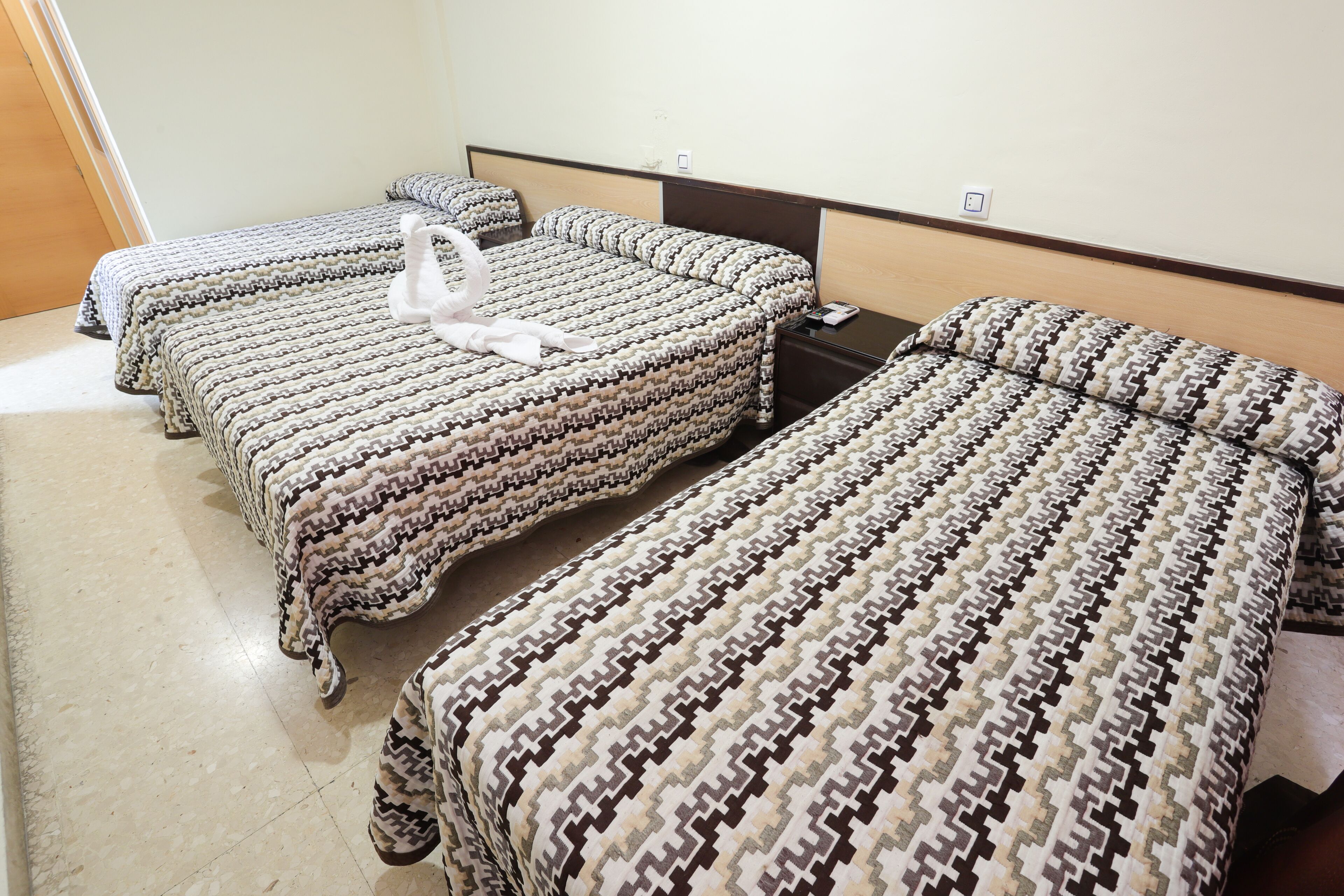 Quarto de hotel com três camas, cada uma com roupa de cama estampada e uma toalha branca.