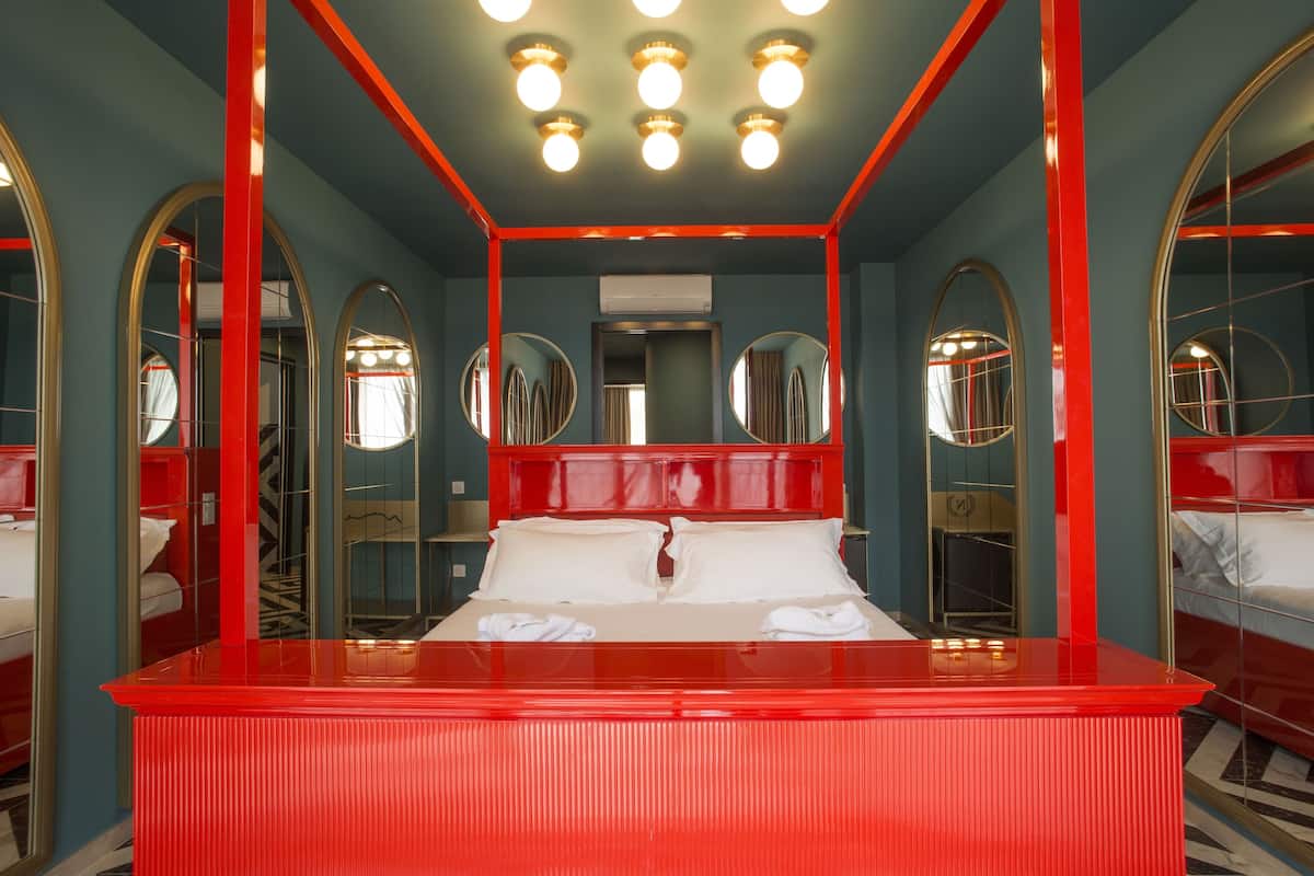 Une pièce avec un lit rouge, de nombreux miroirs et un plafond orné de luminaires.