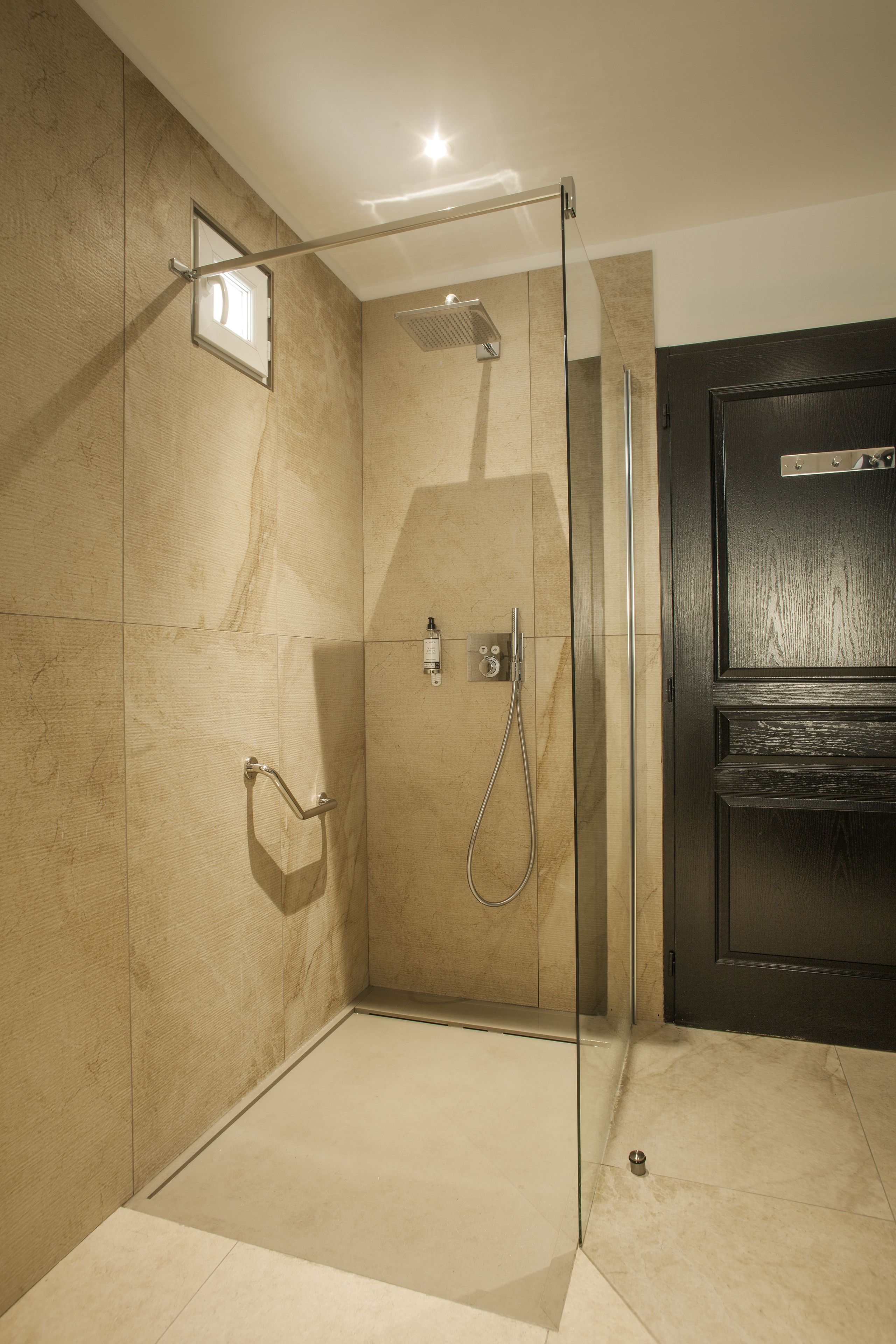 Un área de ducha moderna con puerta de vidrio, un cabezal de ducha de mano y panel de control en la pared.