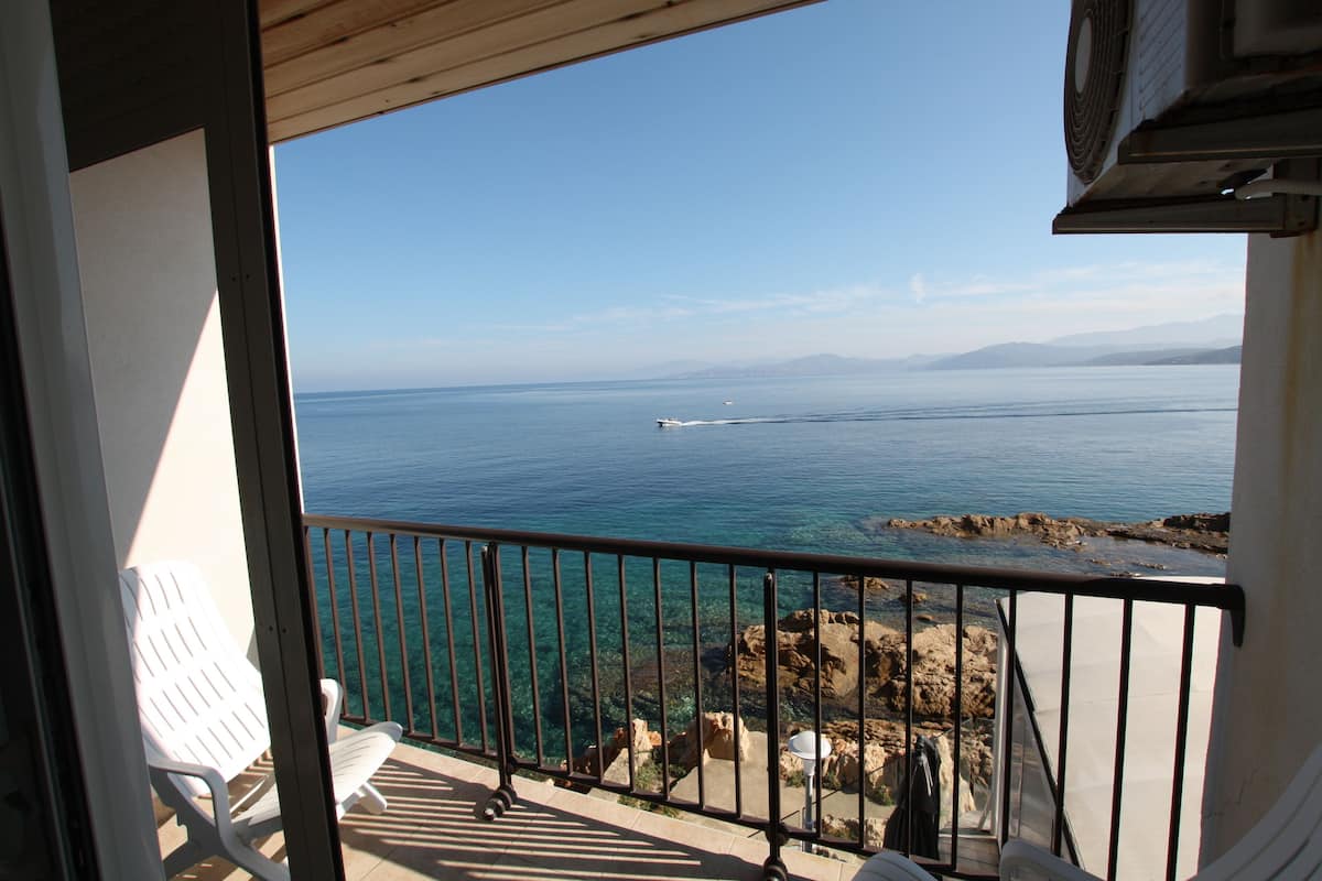 Un balcon avec vue sur la mer, une chaise blanche et une rambarde en métal.