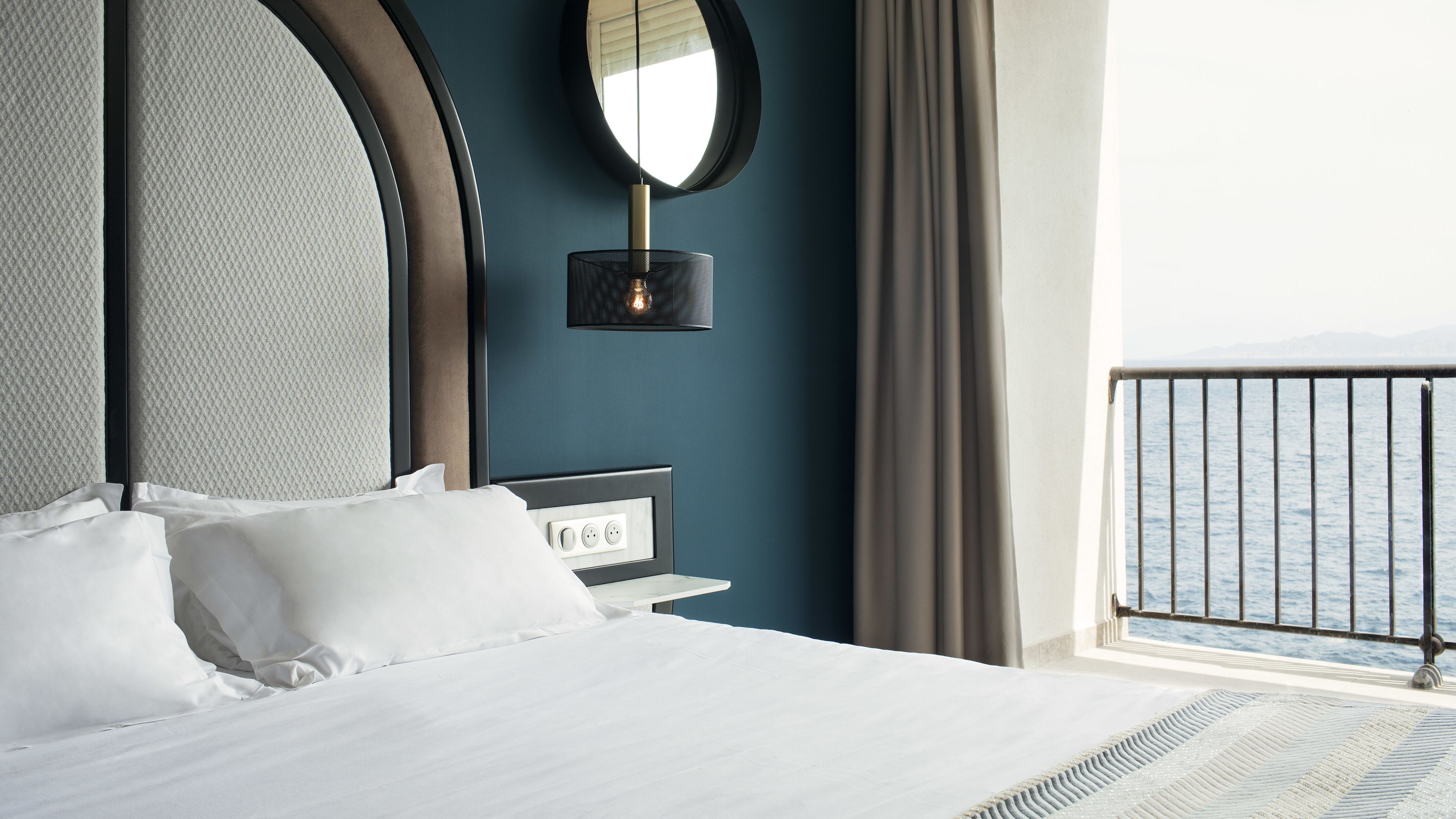Une chambre d’hôtel avec un lit, une table de chevet, un miroir et une vue sur la mer.