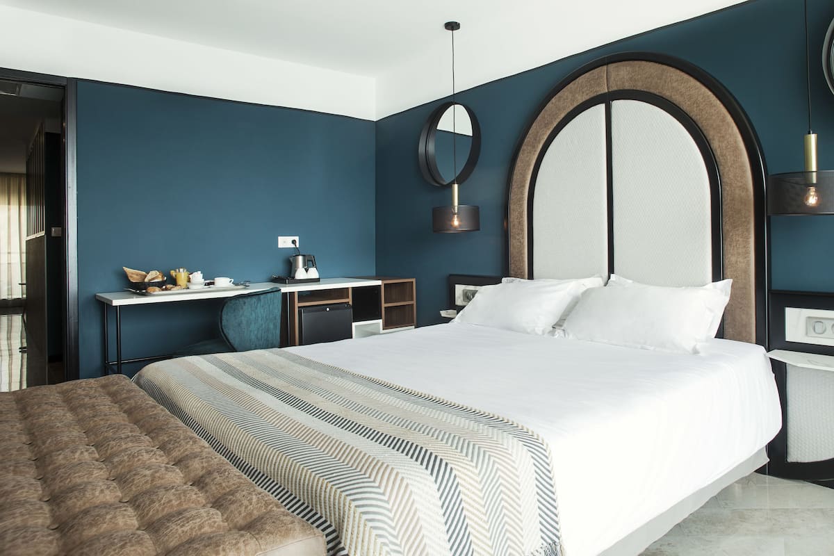 Une chambre d’hôtel moderne avec un grand lit, un bureau doté d’une bouilloire, un petit meuble et un miroir au mur.