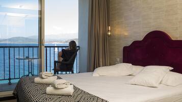 Camera d'albergo con un letto grande, vista sul mare, un balcone con una sedia e un tavolo.