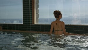 Una persona en una bañera con vistas al mar a través de un ventanal grande.