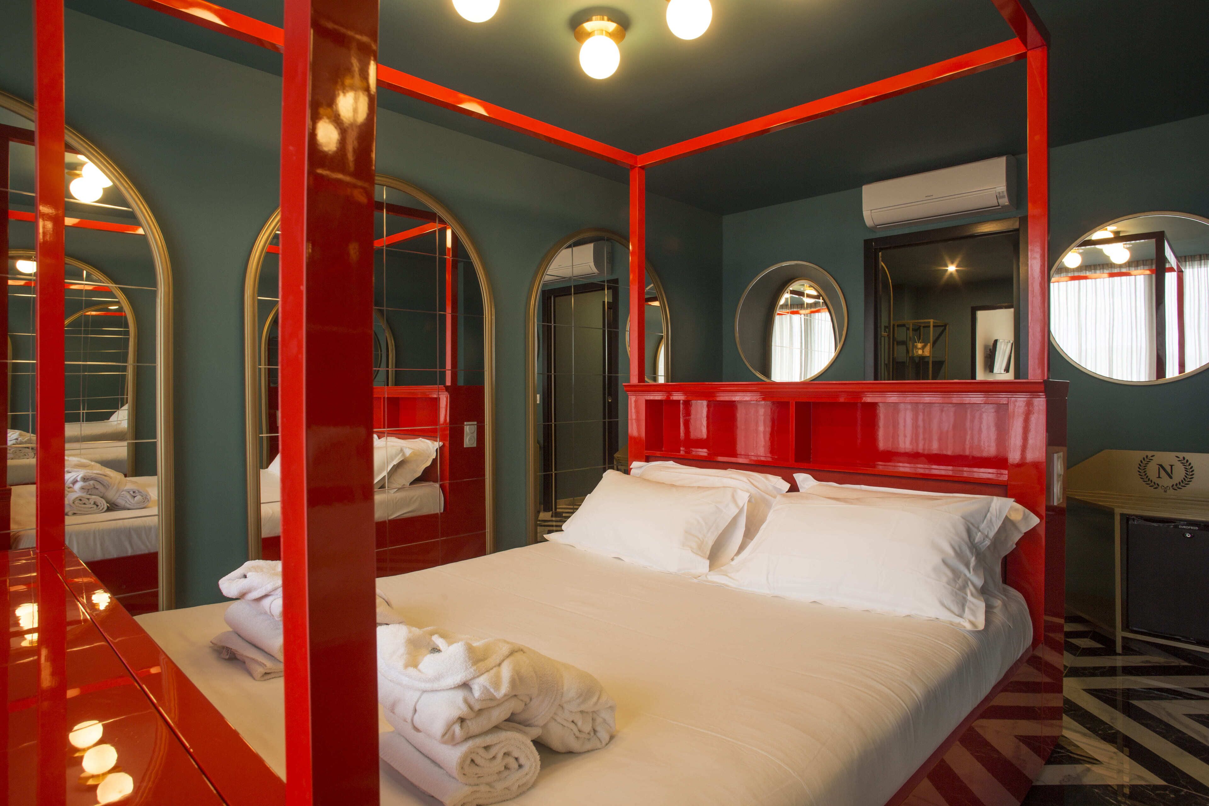 A hotel room with a large bed, red accents, and multiple mirrors.
