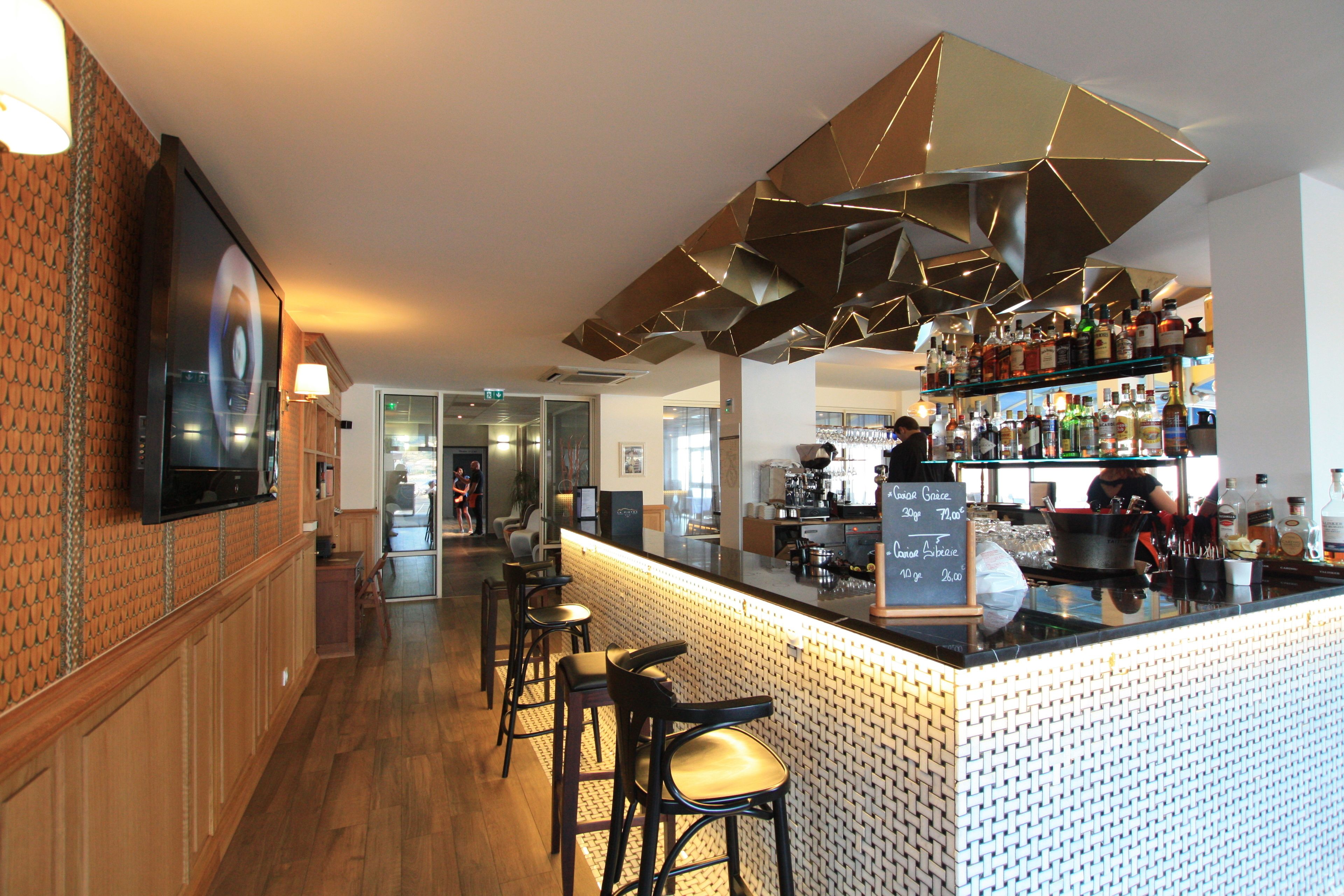 Een bar met een toonbank, krukken en een selectie flessen en glazen.