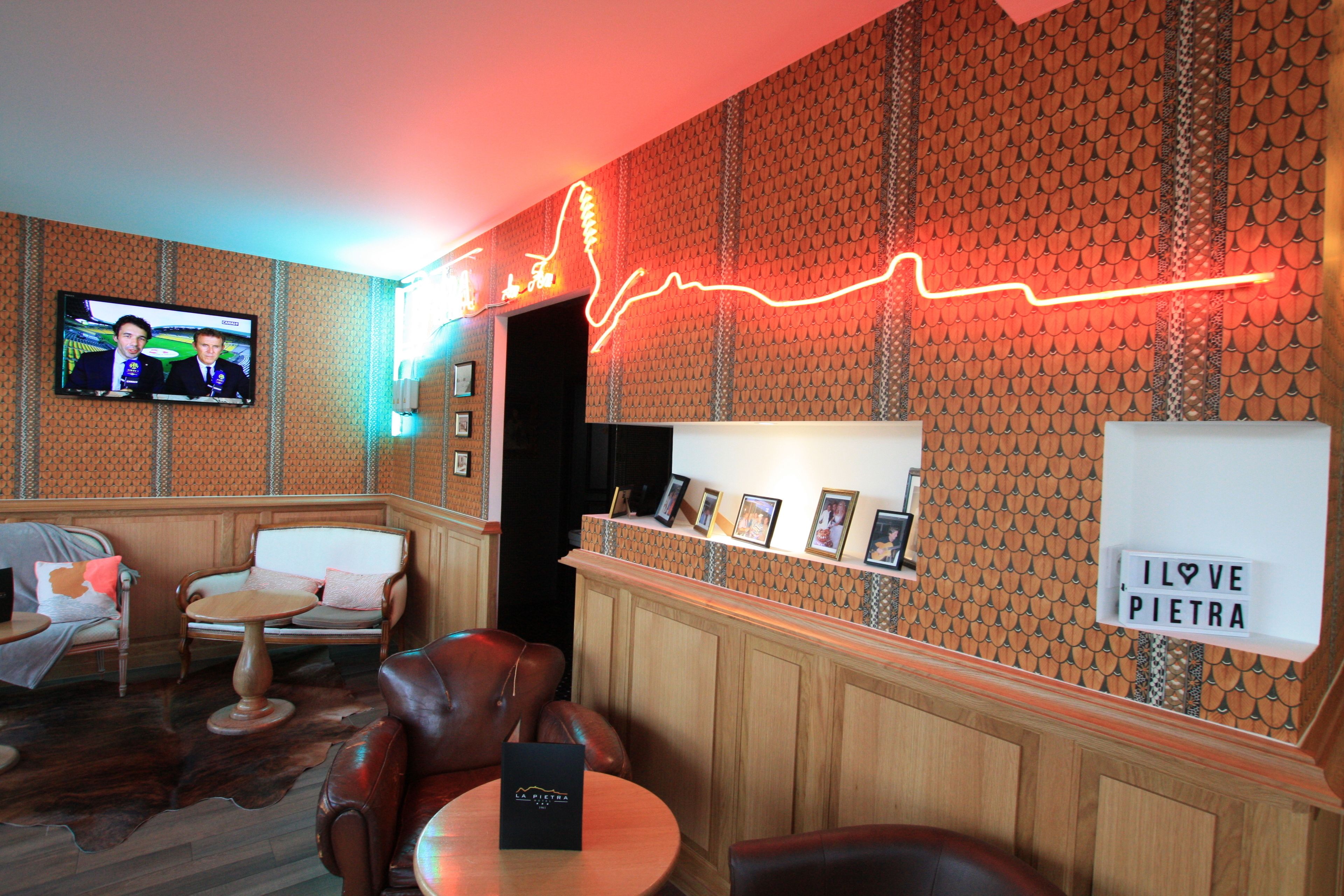 A room with a television, leather chairs, a small table, and a neon light on the wall.