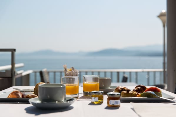 Una mesa de desayuno con croissants, una taza, un vaso de zumo de naranja y un plato de comida, con vistas a un paisaje pintoresco.