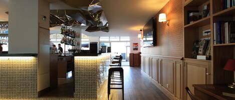 A modern bar area with a counter, stools, and a patterned floor. There are bookshelves and a television on the wall.
