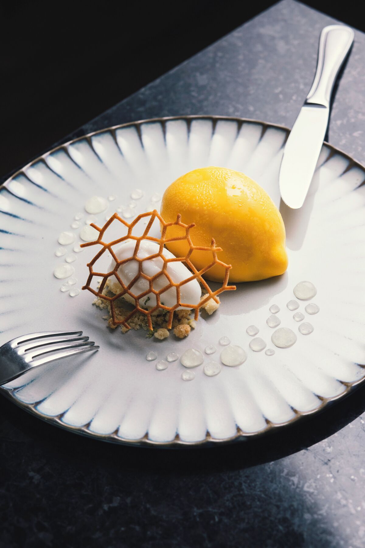 Un dessert su un piatto con una struttura a nido d'ape, un limone e una forchetta.