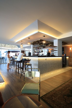 Un bar moderno con una barra alta, taburetes y un área de estar con un tapiz estampado.