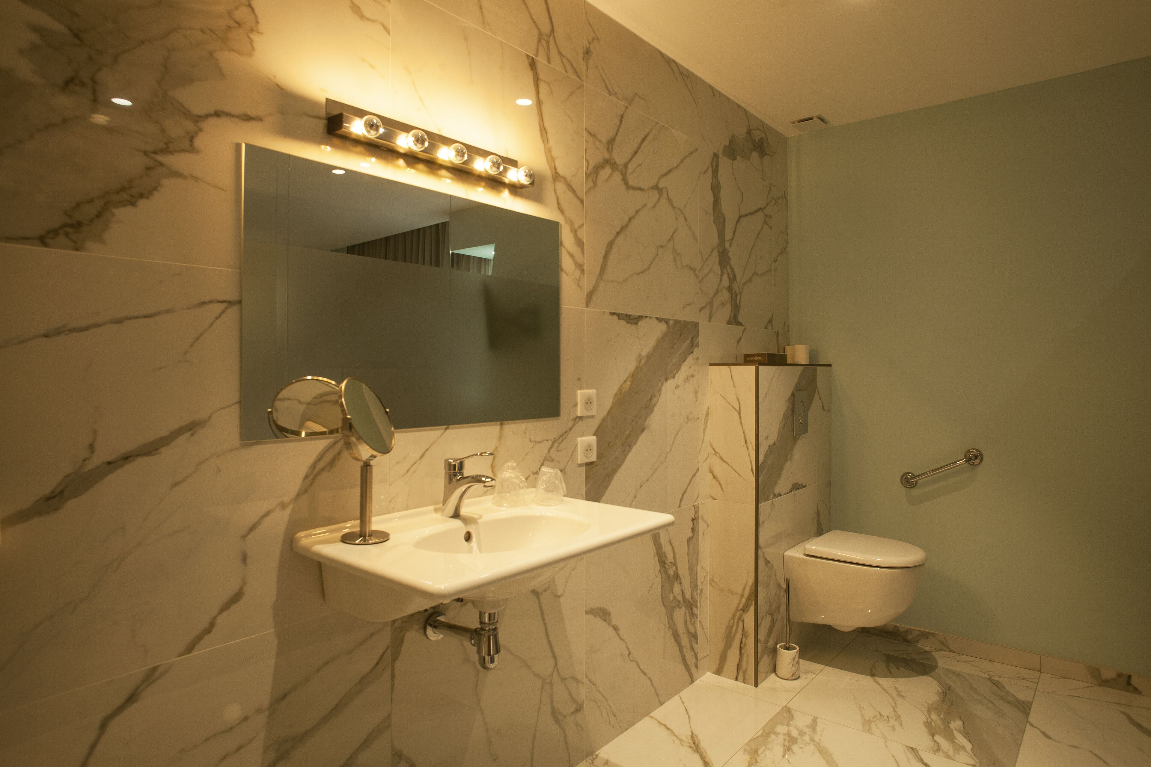 Une salle de bain avec un lavabo en marbre, un miroir avec éclairage intégré, des toilettes et un espace douche.