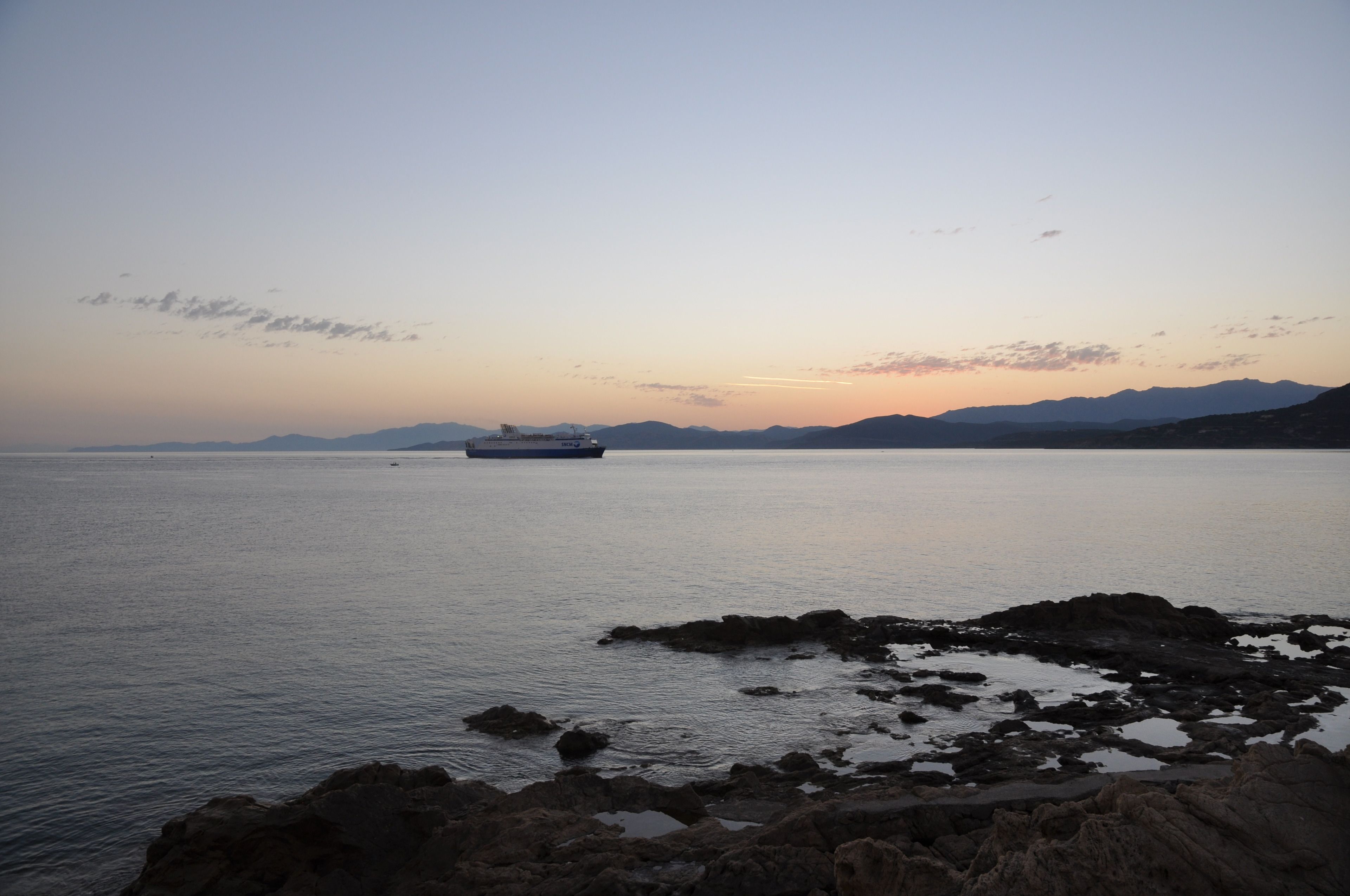 Une mer calme, avec un navire à l'horizon et des côtes rocheuses au premier plan.