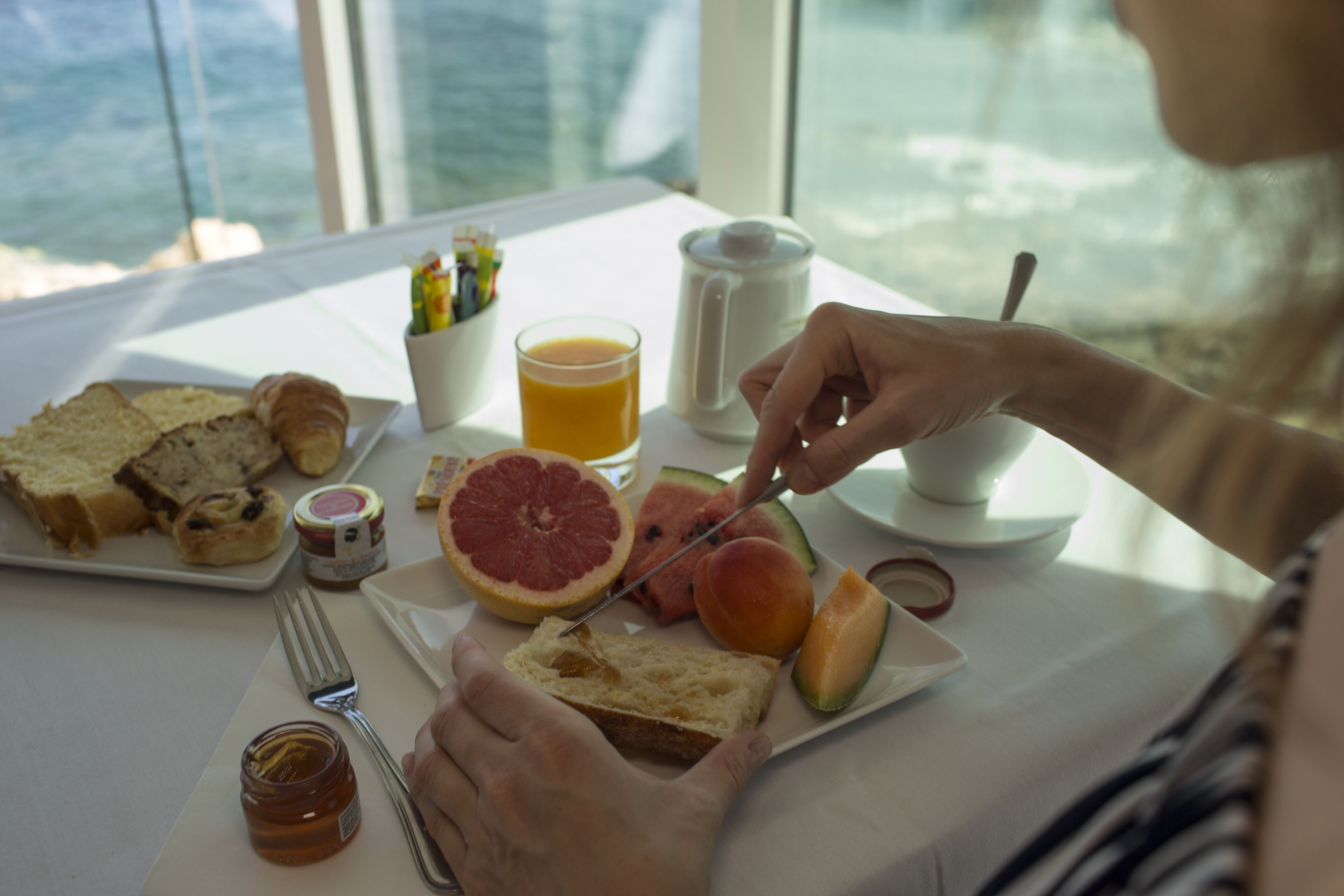 A breakfast setting with toast, fruit, and a coffee pot on a table by a window.