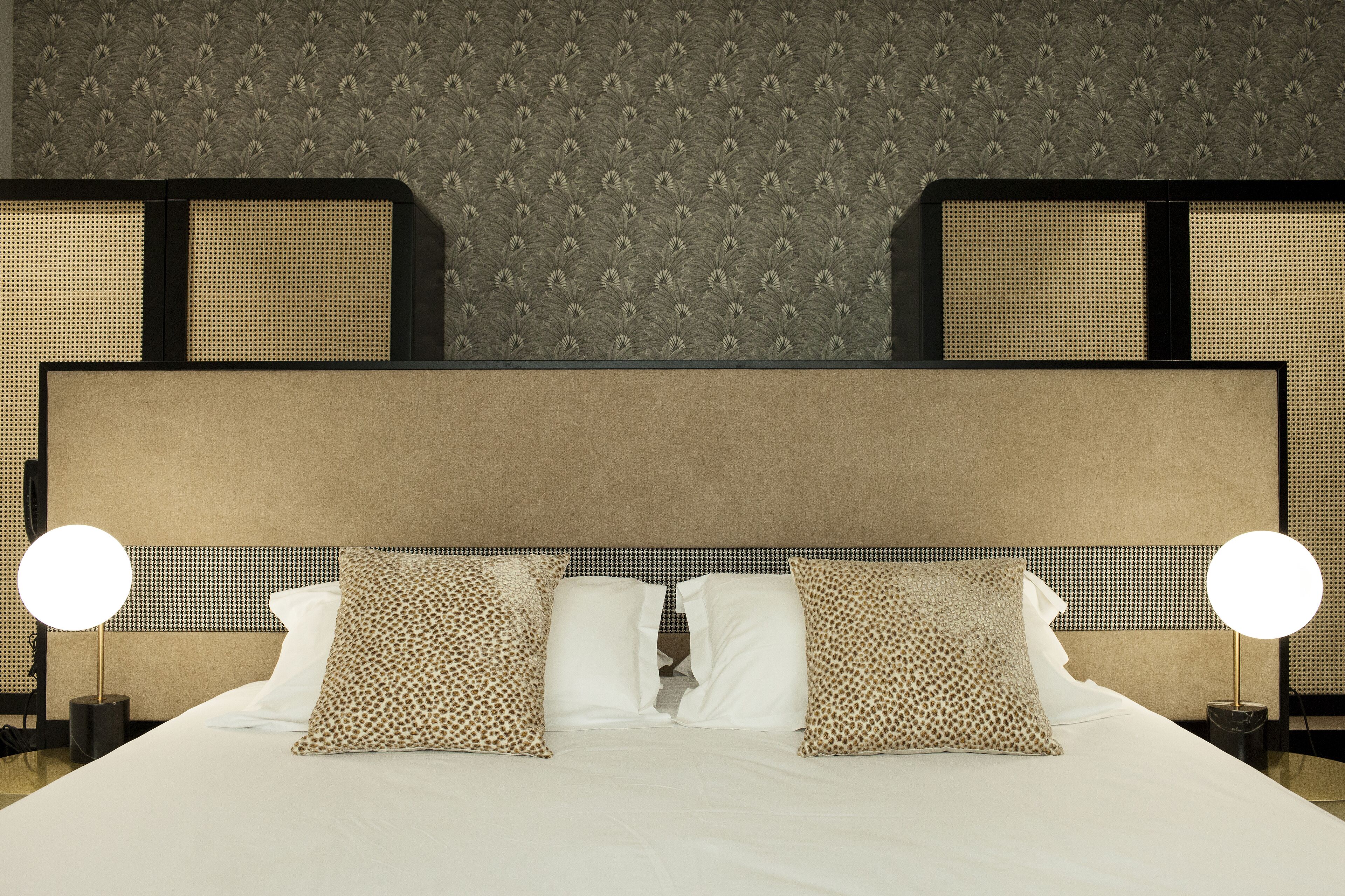 A neatly made bed with a headboard, two bedside lamps, and patterned pillows.