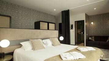 A modern hotel room with a large bed, two bedside lamps, a sofa, and a bathroom visible through an open door.