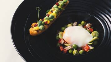 A black plate with a poached egg, peas, and diced vegetables.