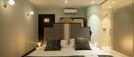 A modern hotel room with a large bed, two bedside tables, a glass shower enclosure, and a wall-mounted air conditioner.
