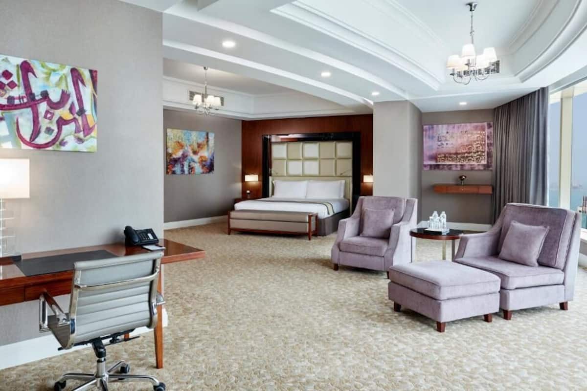 Une chambre d’hôtel comprenant un lit, un bureau, deux fauteuils, une petite table et des œuvres d’art accrochées aux murs.