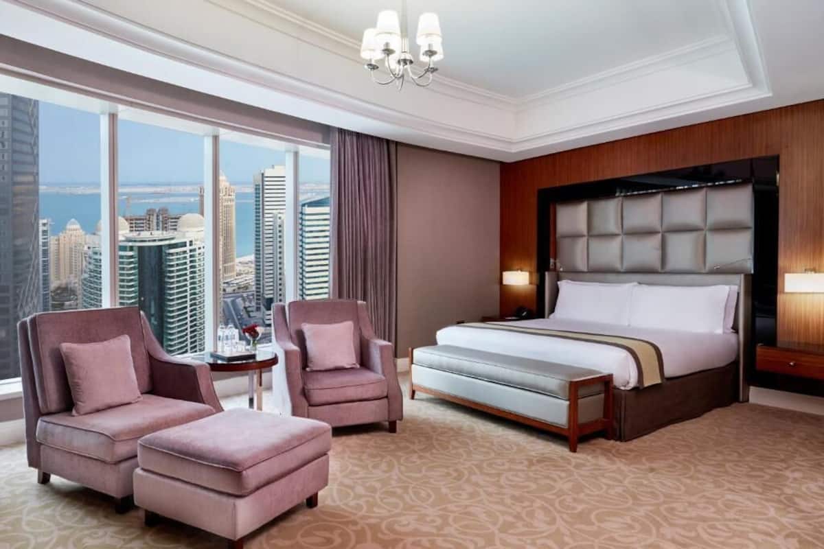 Une chambre d’hôtel avec un grand lit, deux fauteuils, une petite table et une vue sur les bâtiments de la ville.
